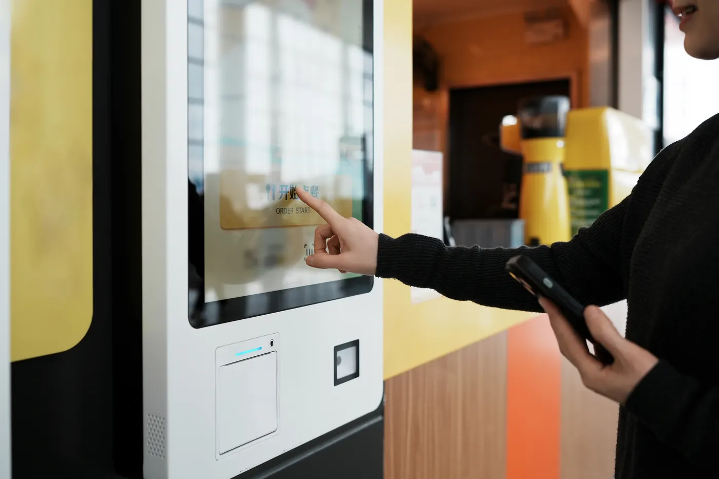 Pessoa usando um totem de autoatendimento com tela touch, leitor e impressora embutidos